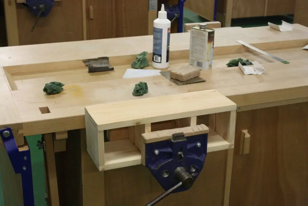 A small timber box held in a bench vice, with glue and clamps on the bench